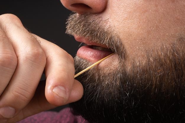 Close up bearded man clean teeth from food stuck her teeth with toothpick after breakfast lunch dinn...