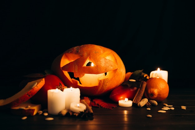 Shiny candles, cinnamon and fallen leaves stand before scarry halloween pumpkin
