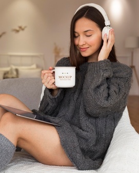 Woman listening to music on headphones while holding a mug mock-up